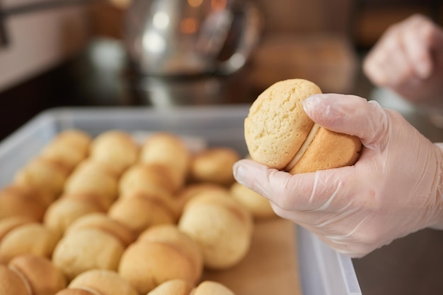 女性の菓子職人が新鮮なマフィンにプラスチックの絞り袋のキャラメルを詰めて、自宅のキッチンでおいしい天然デザートを作ります。上からの眺めをご覧ください。