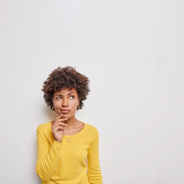 Photo woman considers something concentrated above with pensive expression makes choice decide how to do dressed casually poses on white blank space