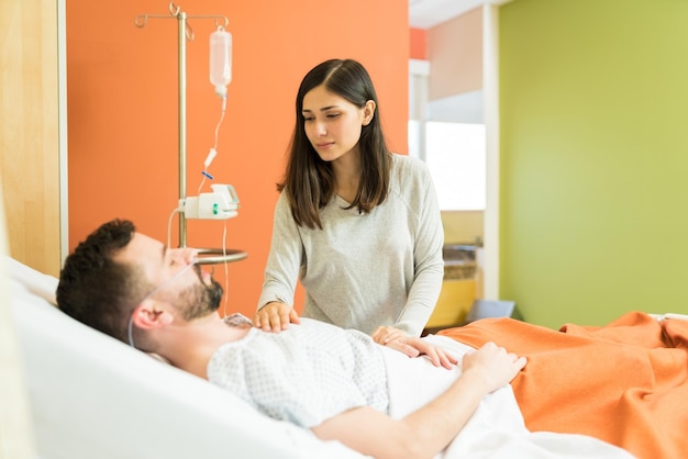 Woman consoling man while standing by bed at hospital