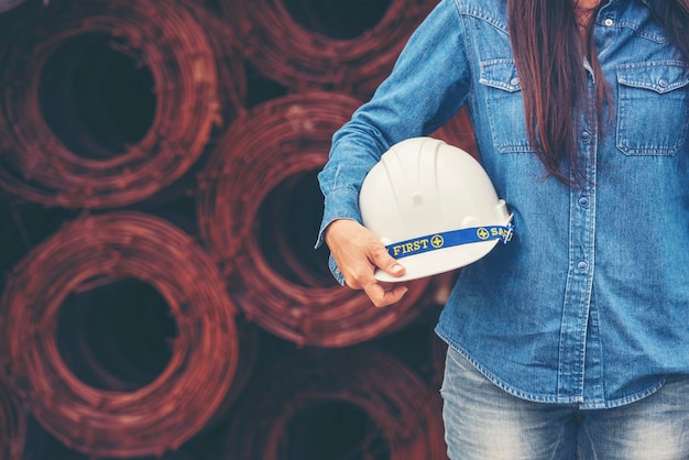 女性の建設エンジニアは、建設現場の産業労働者で安全な白いヘルメットを着用します女性のエンジニア労働者は、ヘルメットの安全ヘルメットを備えた土木工学女性の建設エンジニアのコンセプト