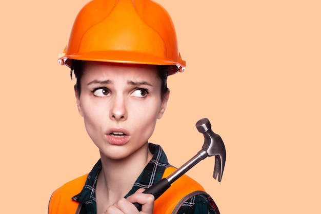 woman in a construction helmet and an orange vest holds a construction tool in her hand