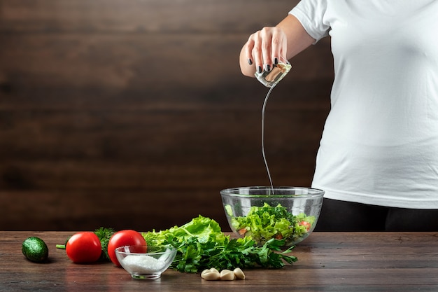 Woman cook adds olive oil to salad, cooking salad on wood. 