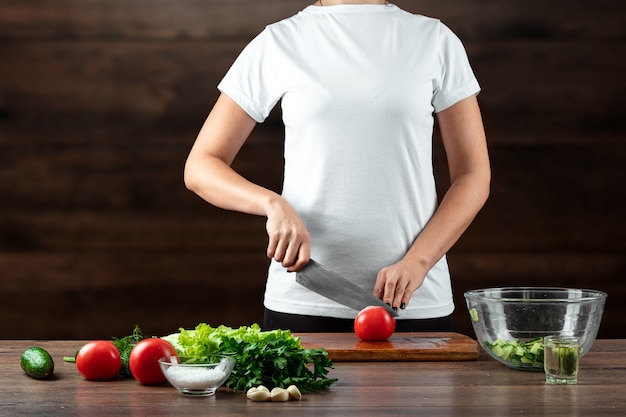 Woman cook cuts vegetables for salad preparation on wood. 