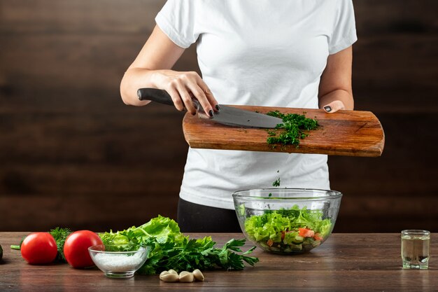 Woman cook cuts vegetables for salad preparation on wood. 