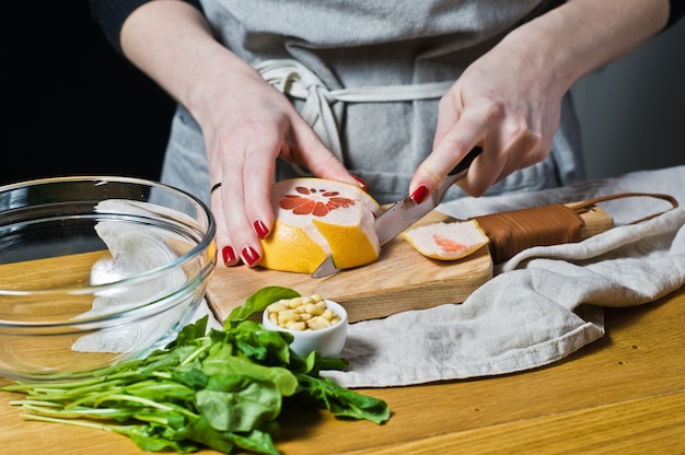 Woman cook grapefruit salad on a wooden cutting Board. 