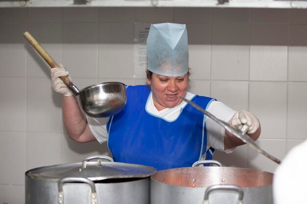 A woman cook in an industrial kitchen with a large ladle among metal pans Chef at the hospital