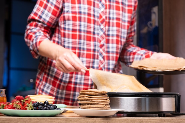 Woman cooking delicious crepe on electric pancake maker in kitchen closeup