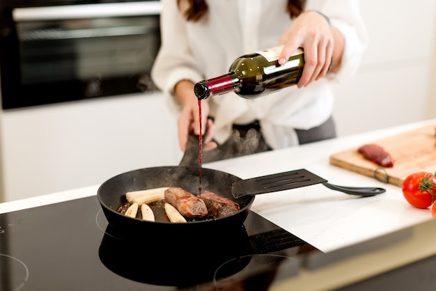 Woman cooking meat with wine on the pan with the steam on the kitchen