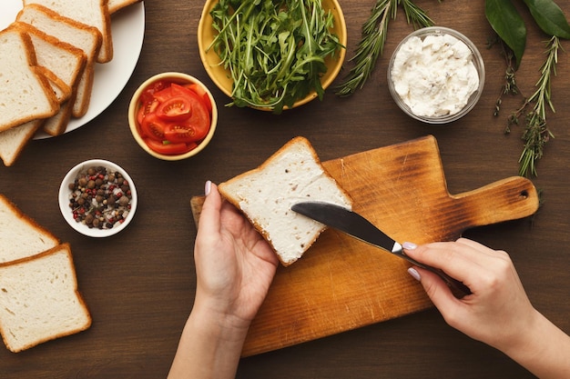 크림 치즈, 최고 전망으로 맛있는 샌드위치를 요리하는 여자. 빵에 브루스케타 토핑을 퍼뜨리는 여성의 손. 건강한 식생활 개념