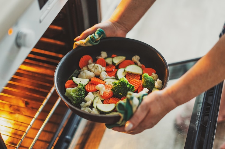 Photo woman cooking vegetables puting pan with vegetables to the oven. home cooking concept.
