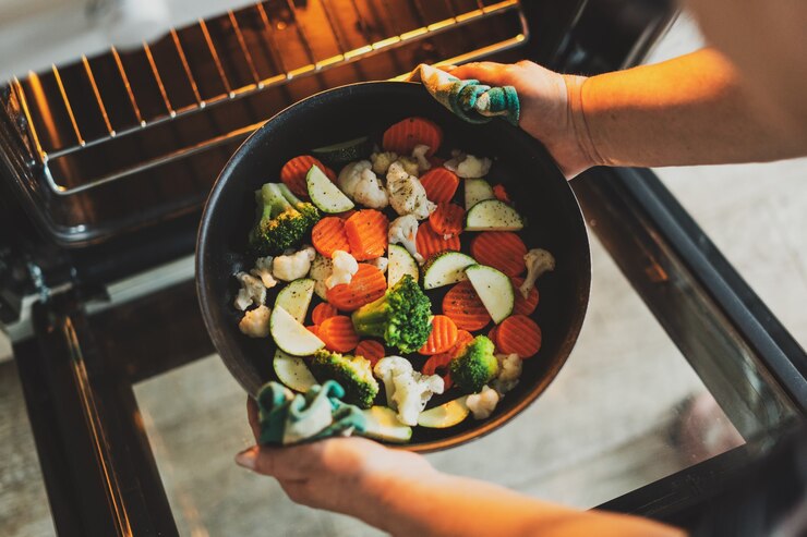 Photo woman cooking vegetables puting pan with vegetables to the oven. home cooking concept.