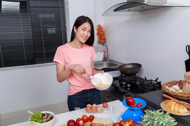 woman cooking and whisking eggs in a bowl in kitchen 