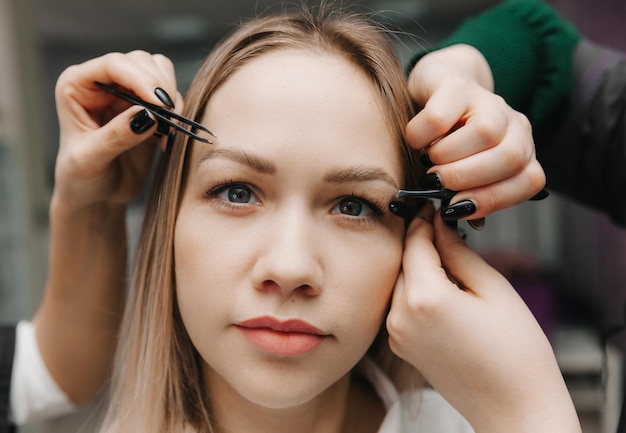 A woman corrects the shape of her eyebrows in a beauty salon 4 hands do eyebrow correction