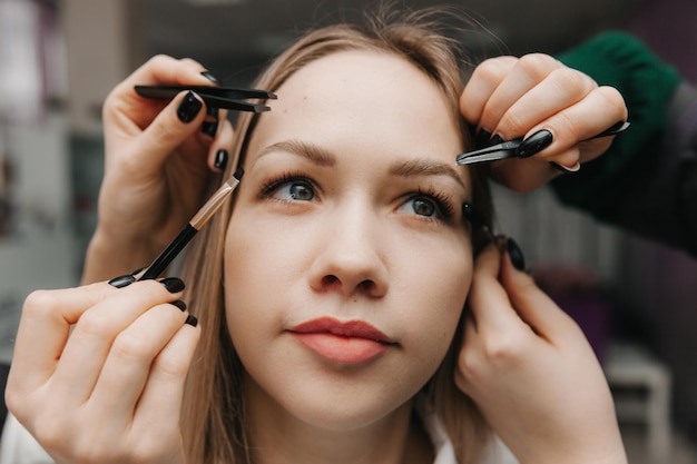 A woman corrects the shape of her eyebrows in a beauty salon 4 hands do eyebrow correction