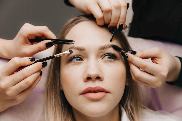 A woman corrects the shape of her eyebrows in a beauty salon 4 hands do eyebrow correction