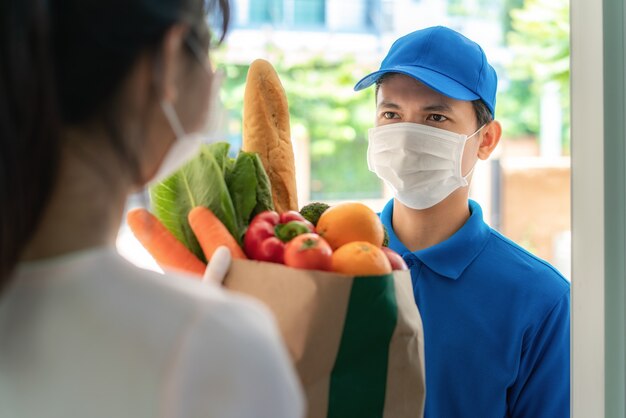 얼굴 마스크와 장갑을 착용하는 여성 costumer는 음식의 식료품 상자를받습니다.