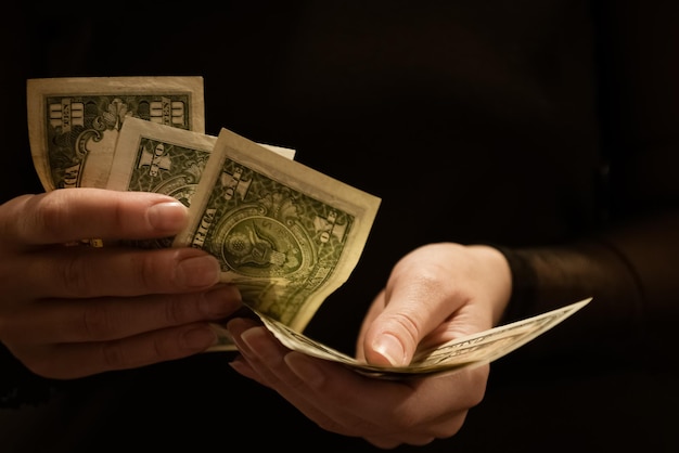Женщина считает банкноты долларов в руках, темный фон