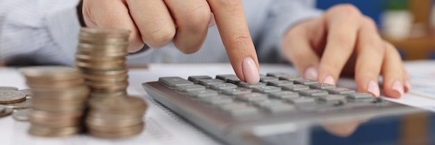 A woman counts on a gray calculator near the coins