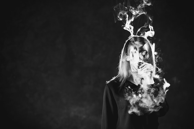 Woman covered in smoke and wearing a mask. Health hazard concept. Toxic influence of smoking addiction.