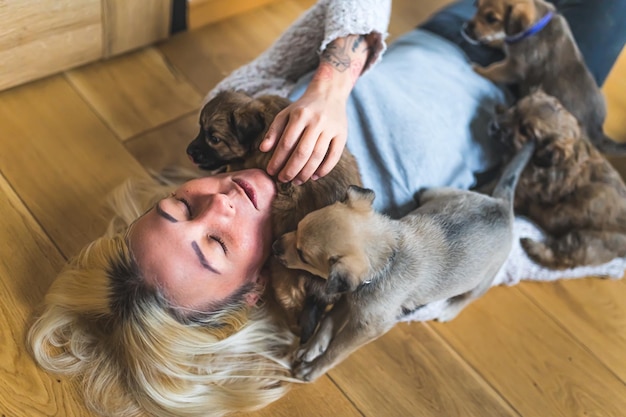 Woman covered with puppies Indoor top view of young adult blond woman with closed eyes lying down on wooden floor covered with adorable brown puppies jumping all over her body Human and animals