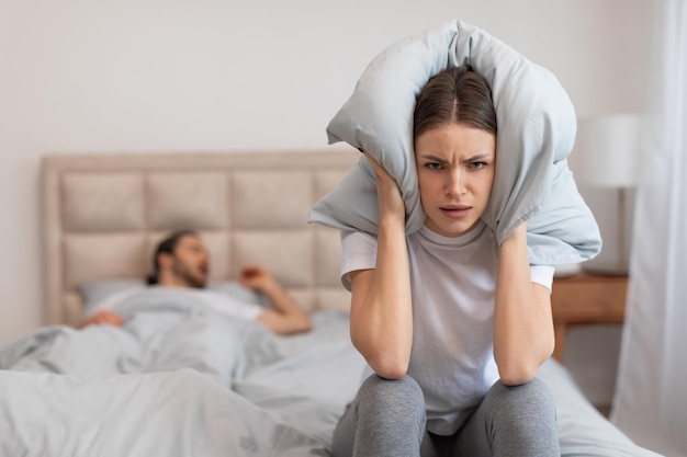 Woman covering ears with pillow man snoring