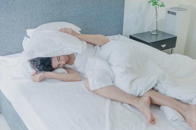 Woman covering ears with pillows while sleeping on bed
