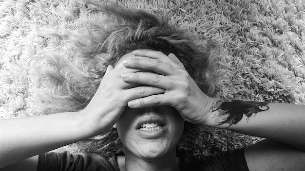 Foto donna che copre gli occhi con le mani mentre giace sul tappeto a casa