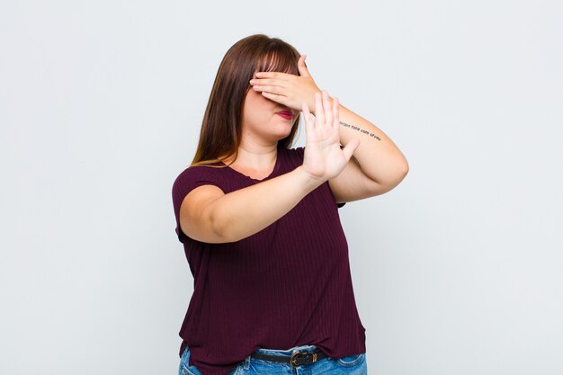 Woman covering face with hand and putting other hand up front to stop camera, refusing photos or pictures