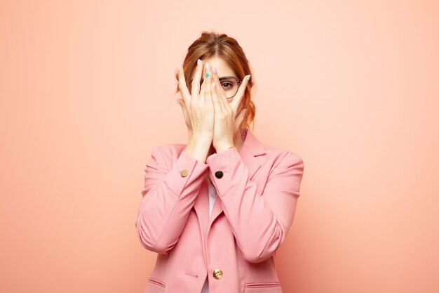 woman covering face with hands, peeking between fingers with surprised expression and looking to the side