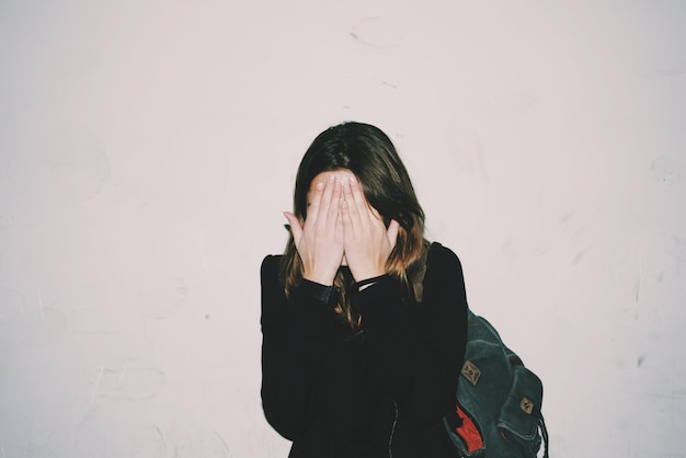 woman covering face with hands standing against wall