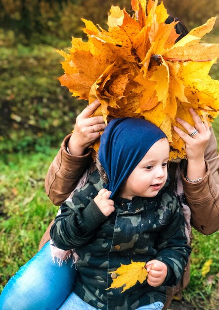 Woman covering face with leaves while sitting by daughter on field