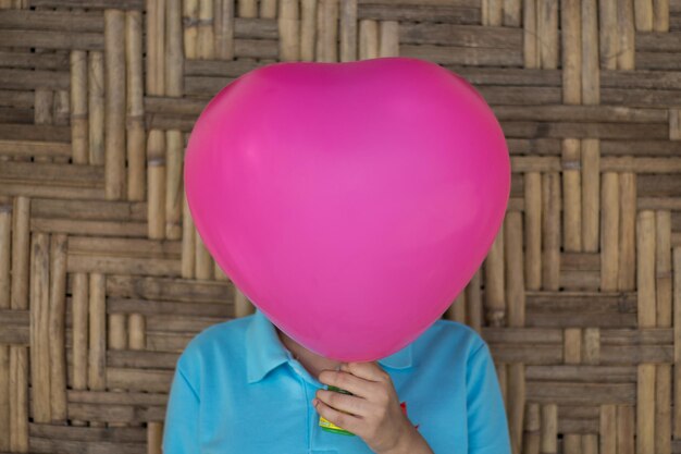 Photo woman covering face with pink balloon against wooden wall