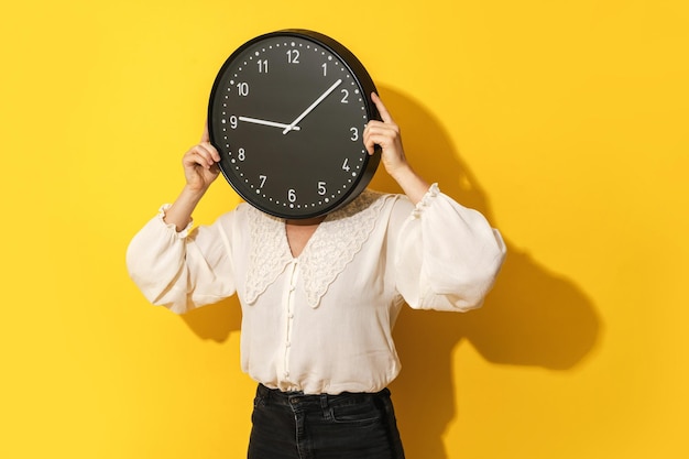 Photo woman covering her face with big clock on yellow background