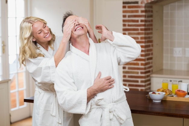 Woman covering her husband eyes in the kitchen