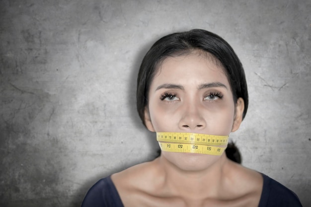 Woman covering her mouth with a measure tape