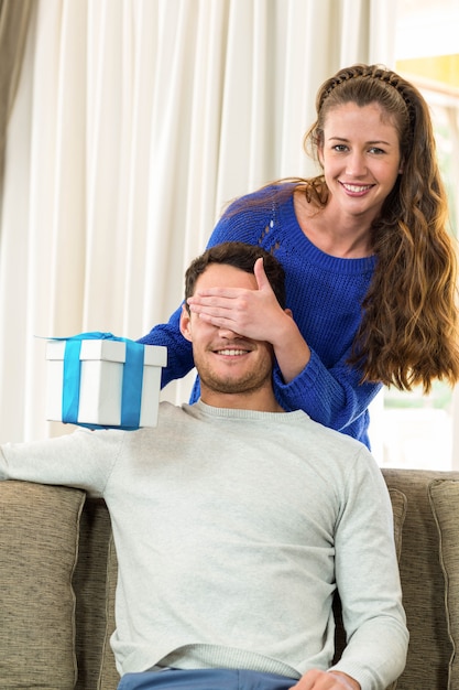 Woman covering mans eyes while giving him a surprise gift