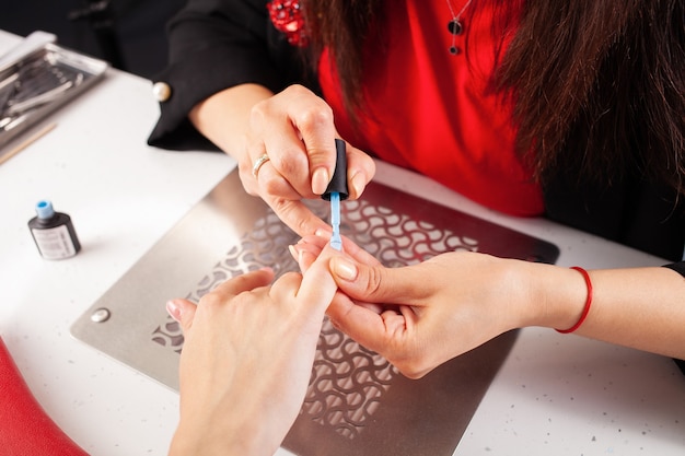 The woman covers the clients nails with blue gel varnish