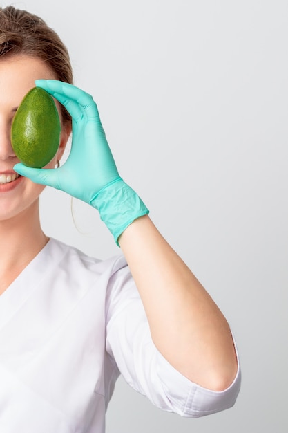Woman covers eye with avocado.