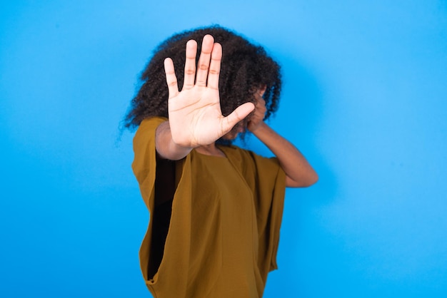 woman covers eyes with palm and doing stop gesture tries to hide from everybody