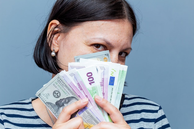 Woman covers face with banknotes on the gray wall