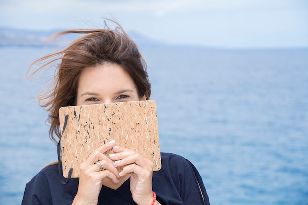 Woman covers her face shyly with her notebook where she has written all her confidences