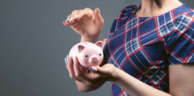 Woman covers piggy bank on gray background