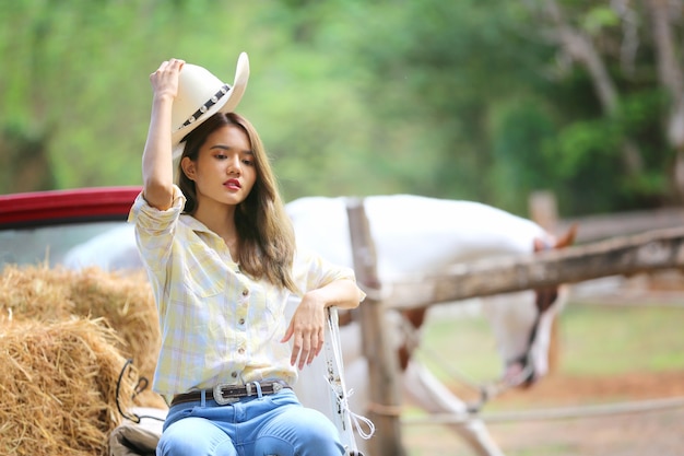 a woman in a cowgirl style sits in a horse ranch with a western farm environment.