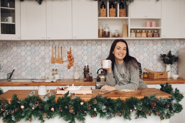 Woman in cozy clothes drinks hot tea in the kitchen