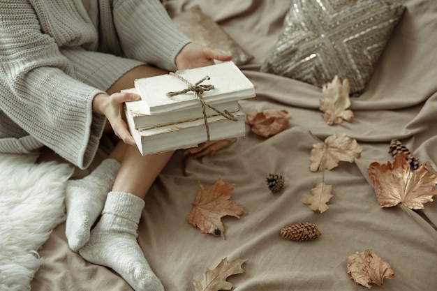 A woman in a cozy knitted sweater lies in bed with a stack of books, autumn mood, blurred background.