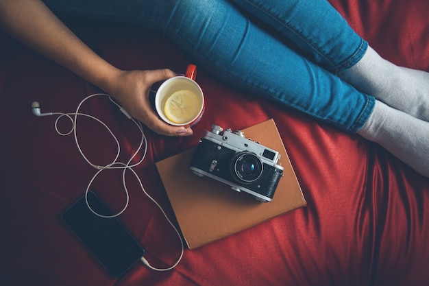 woman in a cozy sweater on the bed with the old book and a cup of tea with milk in their hands, top view