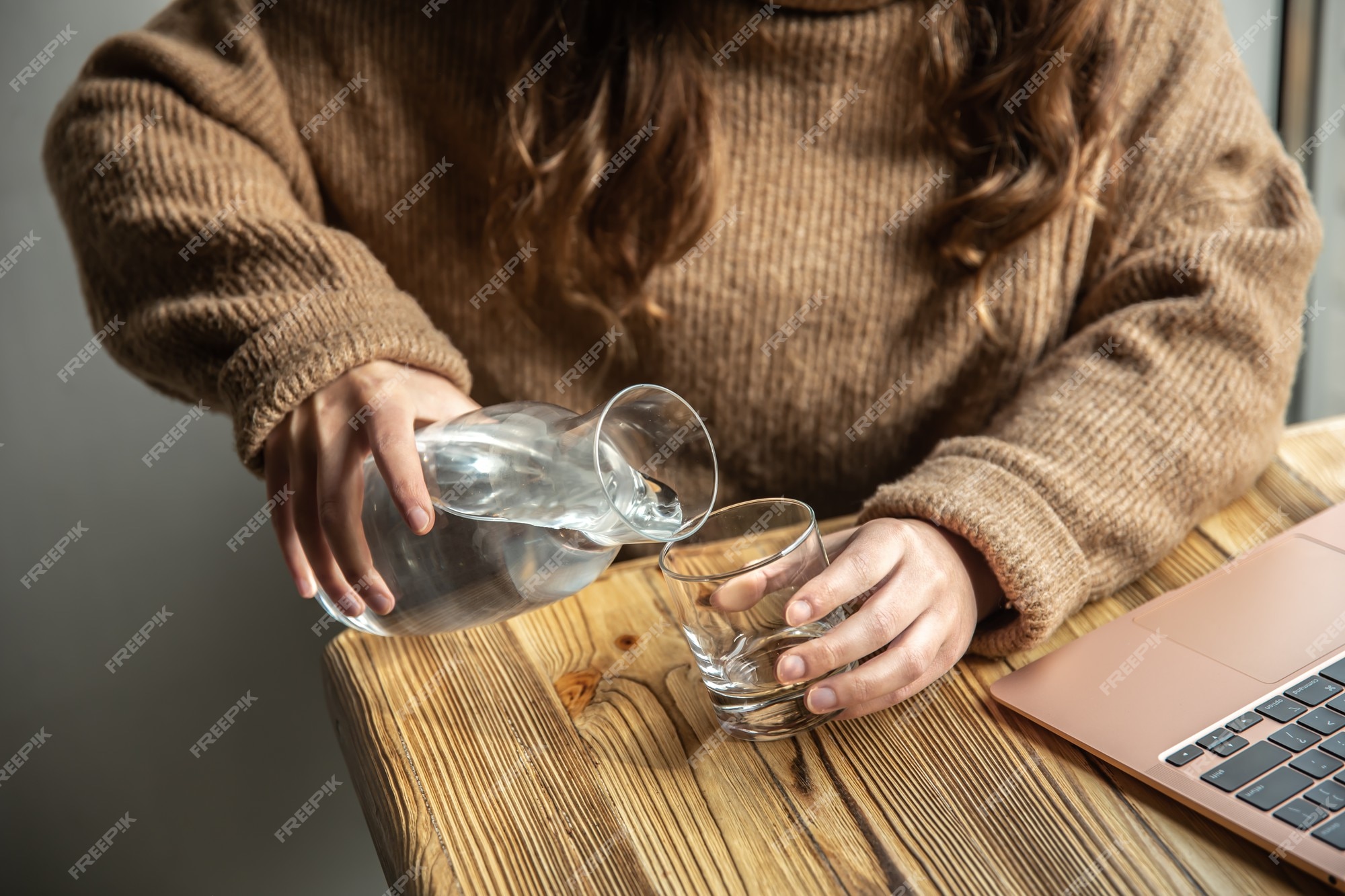 Premium Photo | A woman in a cozy sweater pours water into a glass from a glass decanter, the concept of maintaining water balance.