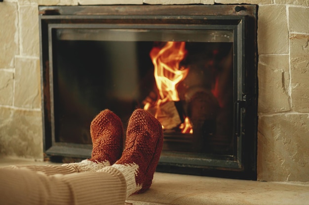 Woman in cozy wool socks warming up feet at fireplace heating
house with wood burning stove