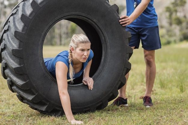 Woman crawling through the tire during obstacle course in boot camp