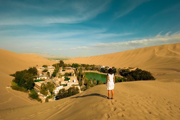 Foto donna che attraversa l'oasi di huacachina nelle dune di sabbia del deserto vicino alla città di ica perù